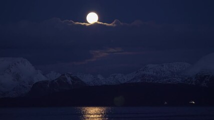 Full moon rising over snow capped mountain range in northern norway, long lens shot