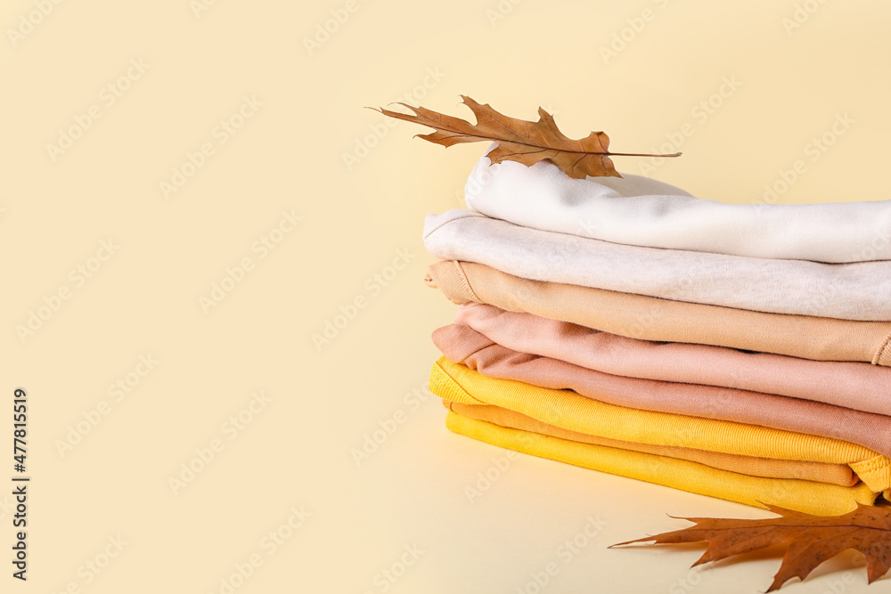 Stack of baby clothes and autumn leaves on color background