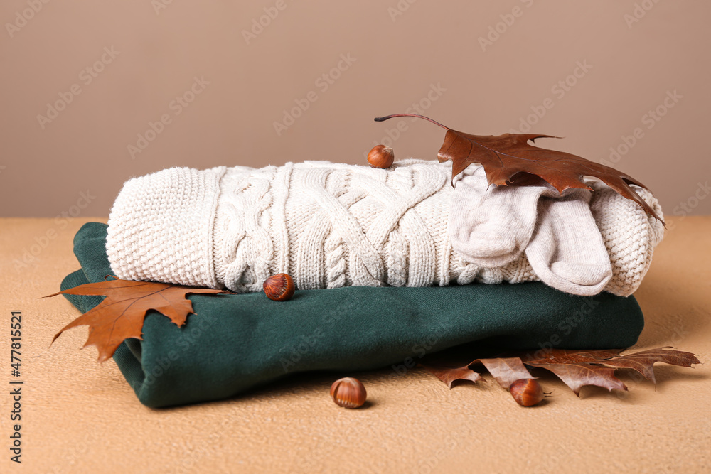 Baby clothes, hazelnuts and autumn leaves on color background