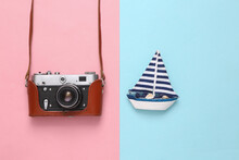 Retro Camera In A Leather Cover And Sailboat On Pink Blue Background. Travel Concept. Flat Lay. Top View
