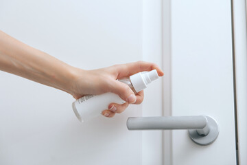 Cleaning white door handles with an antiseptic wet wipe and sanitizer spray. Disinfection in hospital and public spaces against corona virus. Woman hand using towel for cleaning home room door link