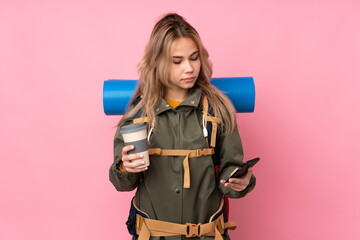 Teenager Russian mountaineer girl with a big backpack isolated on pink background holding coffee to take away and a mobile