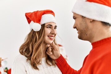 Wall Mural - Young hispanic couple smiling happy wearing christmas hat at home.