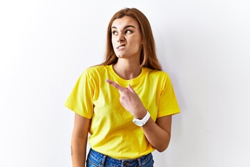 Wall Mural - Young brunette woman standing over isolated background pointing aside worried and nervous with forefinger, concerned and surprised expression