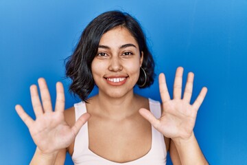 Canvas Print - Young hispanic woman standing over blue background showing and pointing up with fingers number ten while smiling confident and happy.