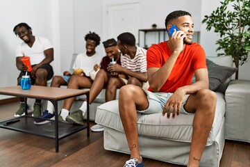 Poster - Group of african american people sitting on the sofa at home. Man smiling happy talking on the smartphone.