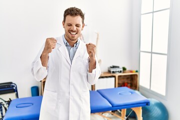 Sticker - Handsome young man working at pain recovery clinic excited for success with arms raised and eyes closed celebrating victory smiling. winner concept.