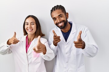 Sticker - Young hispanic doctors standing over white background pointing fingers to camera with happy and funny face. good energy and vibes.