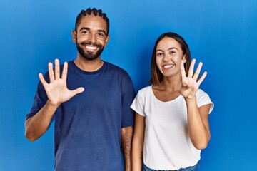 Sticker - Young hispanic couple standing together showing and pointing up with fingers number nine while smiling confident and happy.