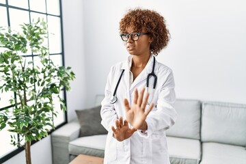 Poster - Young african american woman wearing doctor uniform and stethoscope disgusted expression, displeased and fearful doing disgust face because aversion reaction. with hands raised