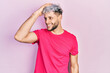 Young hispanic man with modern dyed hair wearing casual pink t shirt smiling confident touching hair with hand up gesture, posing attractive and fashionable