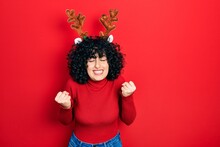 Young Middle East Woman Wearing Cute Christmas Reindeer Horns Very Happy And Excited Doing Winner Gesture With Arms Raised, Smiling And Screaming For Success. Celebration Concept.
