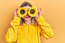 Beautiful Caucasian Woman Holding Yellow Sunflowers Over Eyes Relaxed With Serious Expression On Face. Simple And Natural Looking At The Camera.