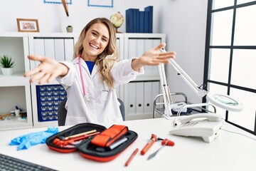 Poster - Young beautiful doctor woman with reflex hammer and medical instruments looking at the camera smiling with open arms for hug. cheerful expression embracing happiness.