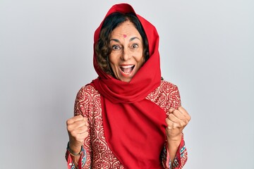 Poster - Middle age hispanic woman wearing tradition sherwani saree clothes celebrating surprised and amazed for success with arms raised and open eyes. winner concept.