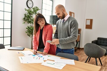 Wall Mural - Two hispanic business workers with serious expression working using smartphone at the office.