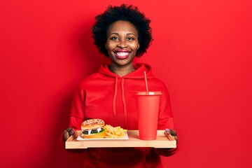 Canvas Print - Young african american woman eating a tasty classic burger with fries and soda smiling with a happy and cool smile on face. showing teeth.