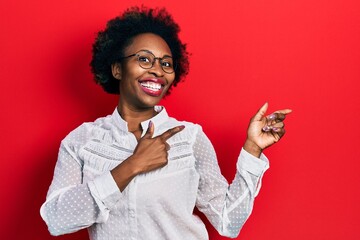 Wall Mural - Young african american woman wearing casual clothes and glasses smiling and looking at the camera pointing with two hands and fingers to the side.