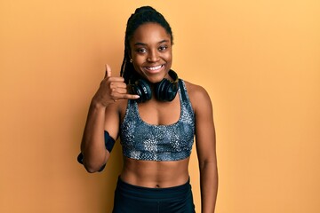 Wall Mural - African american woman with braided hair wearing sportswear and arm band smiling doing phone gesture with hand and fingers like talking on the telephone. communicating concepts.