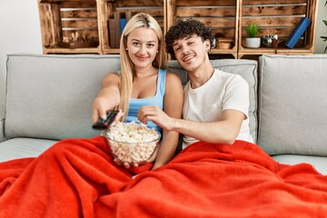 Poster - Young couple watching film and eating popcorn sitting on the sofa at home.