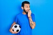 Hispanic man with beard holding soccer ball looking stressed and nervous with hands on mouth biting nails. anxiety problem.