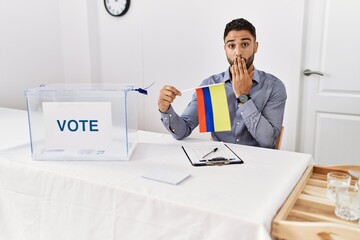 Sticker - Young handsome man with beard at political campaign election holding colombia flag covering mouth with hand, shocked and afraid for mistake. surprised expression