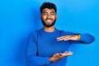 © Krakenimages.com - Arab man with beard wearing casual blue sweater gesturing with hands showing big and large size sign, measure symbol. smiling looking at the camera. measuring concept.