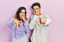 Young Hispanic Couple Wearing Casual Clothes Laughing At You, Pointing Finger To The Camera With Hand Over Mouth, Shame Expression