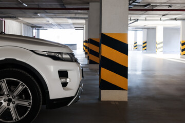 Wall Mural - White car near column with warning stripes in parking garage