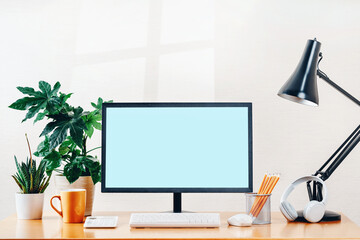 Front view of workspace with modern computer wireless headphones and office supplies. Mockup blue screen for your text or advertising content. Table lamp, calculator. mug, Plant. working from home