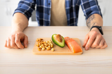 Healthy fat, protein diet and culinary concept. Mature man showing cutting board with salmon fillet, avocado and nuts