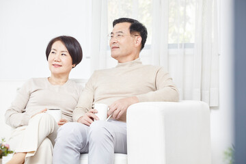 A middle aged couple relaxing while drinking coffee sitting on the sofa living room at home