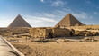The great Egyptian pyramids against the blue sky. The ruins of an ancient temple are visible in the foreground. A sunny day. Giza