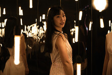 Young Asian Woman Pose And Look At Camera On A Room Full Of Lights And Mirrors.