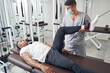Experienced physiotherapist applying gym equipment for patient leg rehabilitation
