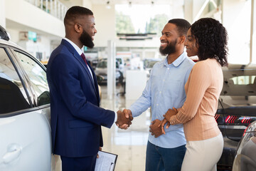 Wall Mural - Sales Manager Helping Black Couple Choose New Car In Modern Dealership Center