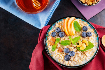 Oatmeal porridge with yogurt, berries and nuts on a linen napkin. Bowl with oatmeal, blueberries, apples and honey on a dark background. Healthy food. Top view. Copy space