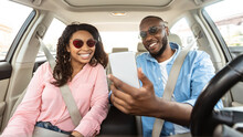 Happy Black Couple Driving Car And Using Smartphone