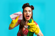Crazy young pinup housewife wearing retro outfit and rubber gloves, holding spray detergent and rag over blue background