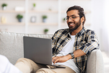 Happy indian guy working from home, using notebook