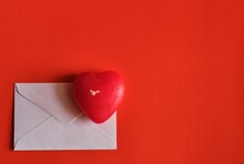Concept For Valentine's Day. A Envelope With Valentine Card And A Heart-shaped Candle On A Red Background With Space For Text Or Logo.