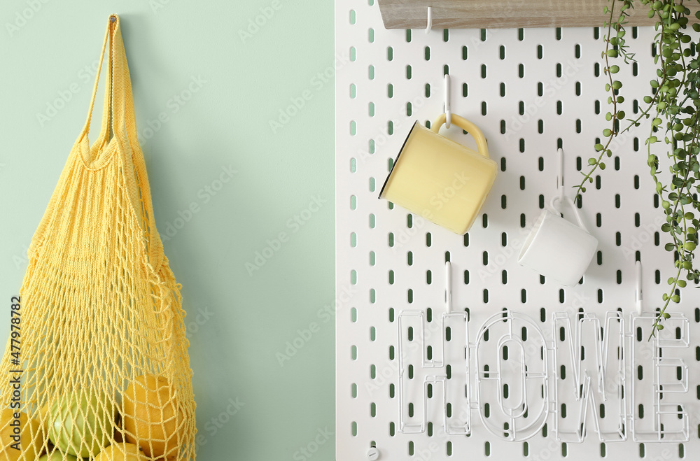 Peg board with cups and string bag hanging on green wall