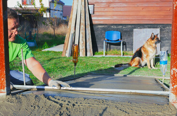 improvement of the yard, a man evens out the concrete solution on the path with the rule