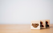 © Dilok - Hand shaking which print screen on wooden cube block  in front of human icon for business deal and agreement concept.