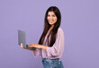 Portrait of confident armenian woman holding and using laptop computer isolated over purple studio background