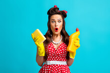Shocked Pinup Woman In Polka Dot Dress Holding Toilet Detergent And Sponge, Making Surprised Face On Blue Background