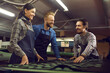 © Studio Romantic - People working in shoe manufacturing workshop. Group of happy young footwear factory workers checking shoe details and talking standing at table near cutting machine