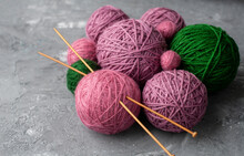 Bulk Of Pink, Purple And Green Balls Of Yarn With Knitting Needles On Grey Background