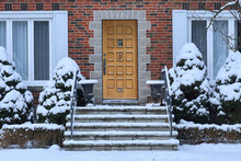 Traditional Brick House With Wood Grain Front Door And Snow Covered Shrubbery