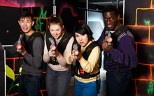 Happy Adult People Of Different Nationalities With Laser Pistols Posing Together On Dark Laser Tag Labyrinth.
